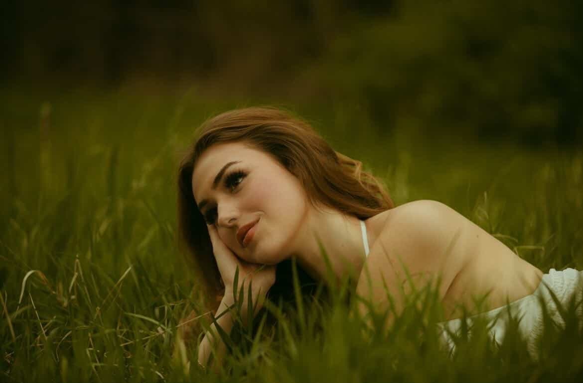 Elena resting in tall grass, head on her hand, smiling softly