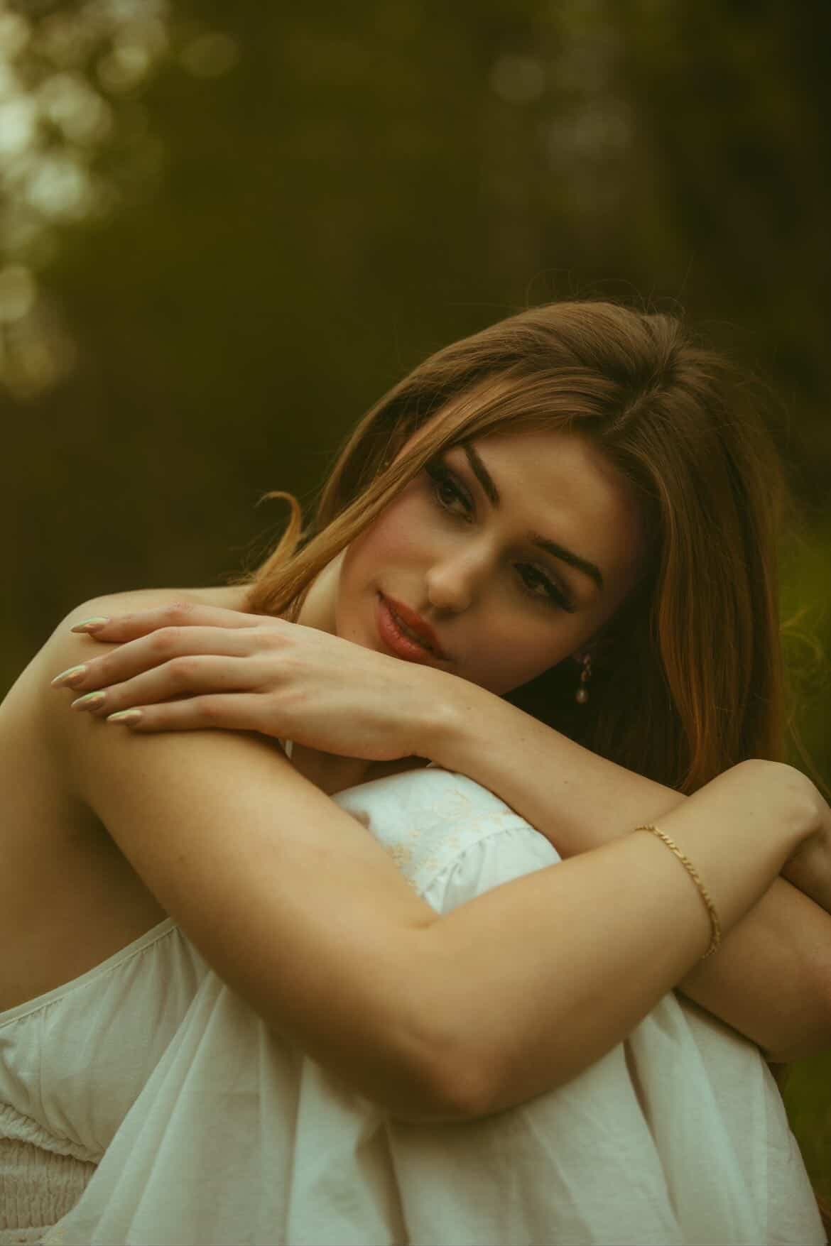 Elena seated with her arms wrapped around her knees, gazing aside