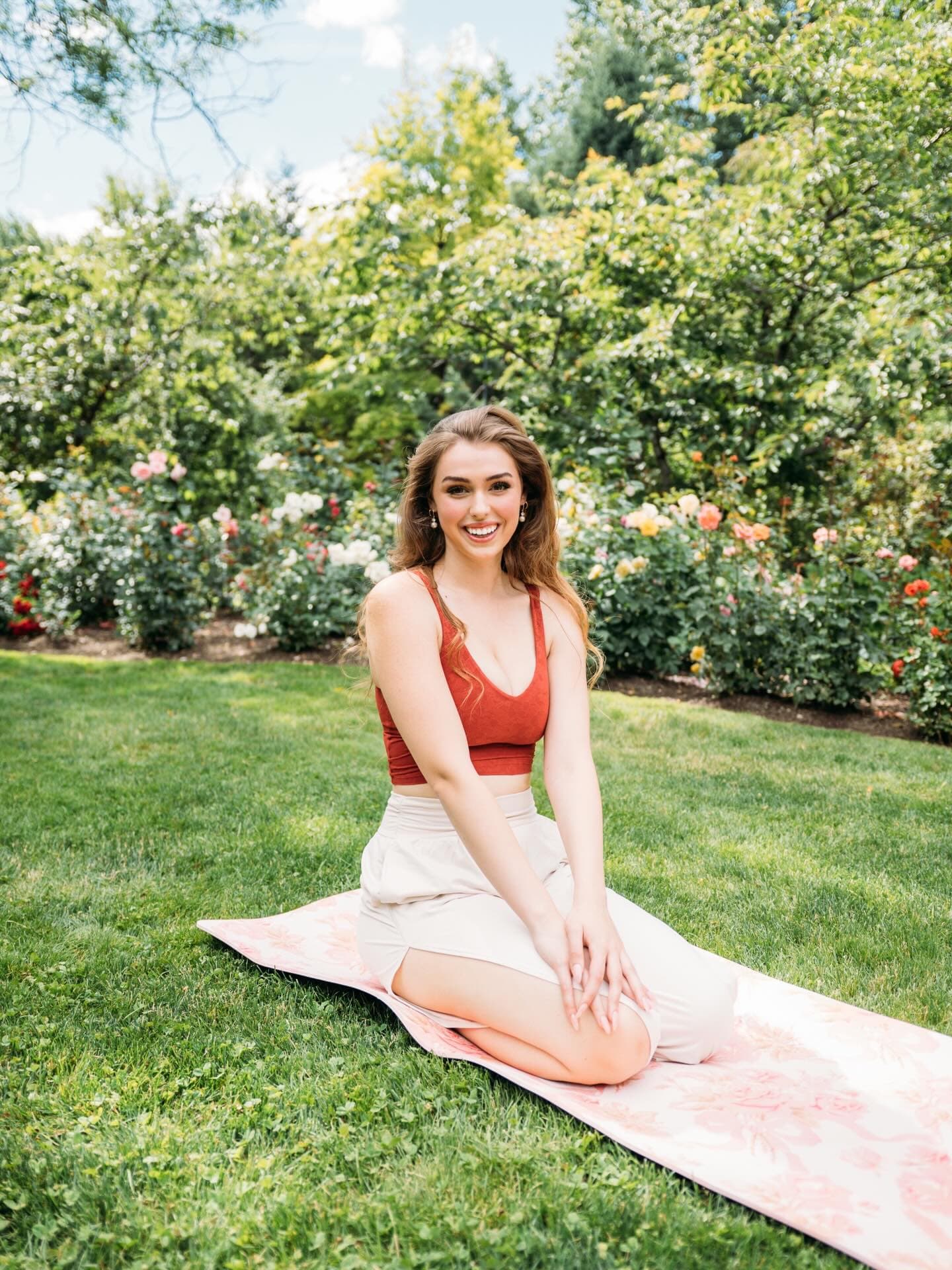 Elena Collins seated on a yoga mat in a rose garden